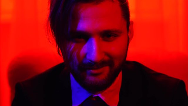 Portrait of bearded smiling man looking in camera. Shooting in red light