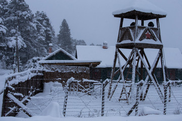 A watchtower with the fence in the middle of the snow covered forest.