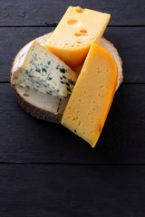 Hard cheese and blue cheese on a wooden stand. Different types of cheese on black boards. Swiss cheese and dorblu on a dark background. Copy space