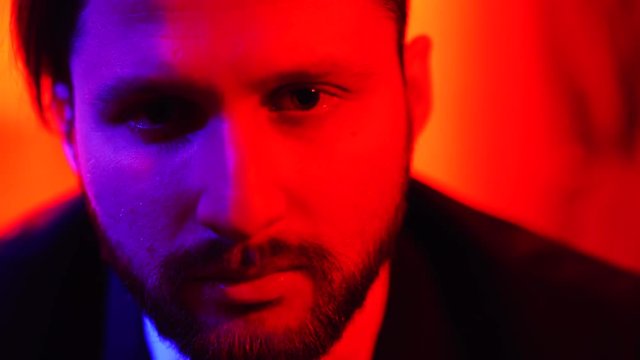 Confused puzzled handsome bearded man standing and looking at camera isolated over bright red light background
