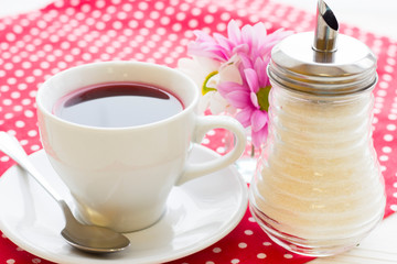 Black tea ceremony - a cup of tea, teapot, flowers on a red with white dots background