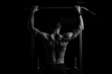Fototapeta na wymiar Power muscular bodybuilder guy doing pullups in gym