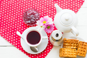 Black tea ceremony - a cup of tea, teapot, sugar, cakes, flowers on a red with white dots background