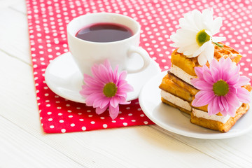 Black tea ceremony - a cup of tea, teapot, sugar, cakes, flowers on a red with white dots background