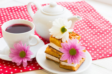 Black tea ceremony - a cup of tea, teapot, sugar, cakes, flowers on a red with white dots background