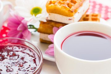 Black tea ceremony - a cup of tea, teapot, sugar, cakes, flowers on a red with white dots background