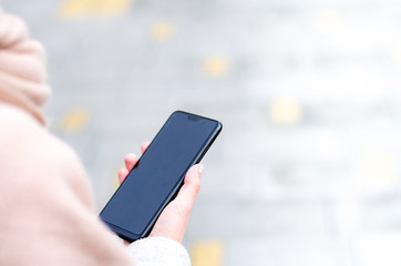 Black blank smart phone in female hand on the street with copy space
