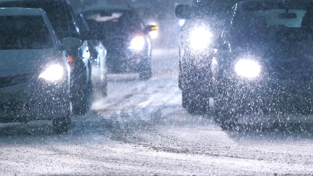 Snow storm in winter city, falling snow illuminated by cars headlights. Slow motion, 4K UHD.