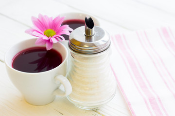 Black tea ceremony - a cup of tea, teapot, sugar, cakes, flowers on white wooden rustic background