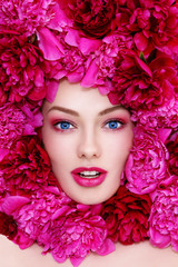 Portrait of young beautiful blue-eyed woman with hot pink peonies around her face