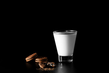 Glass of milk and chocolate cookies on black background