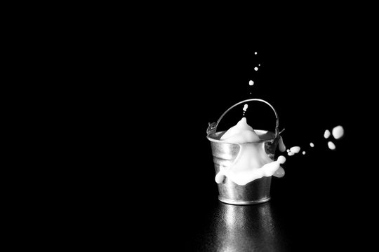 Splash in metal bucket with milk on black background