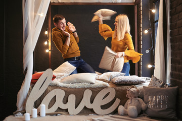 The guy and the girl are fighting with pillows on the bed.