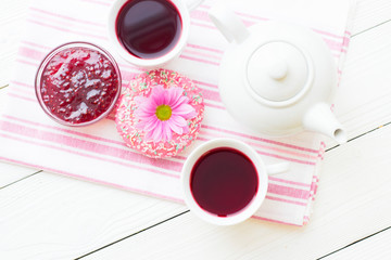 Black tea ceremony - a cup of tea, teapot, sugar, cakes, flowers on white wooden rustic background