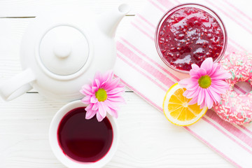Black tea ceremony - a cup of tea, teapot, sugar, cakes, flowers on white wooden rustic background