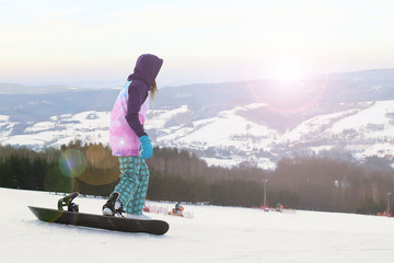 Girl snowboarder stand on the background of snow-capped mountains, preparing for slalom. Modern sports equipment for winter sports. Mountain resort. Physical activity in the open air.