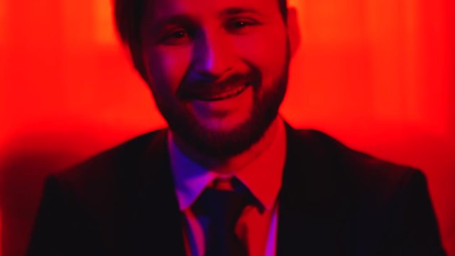 Portrait of bearded smiling man looking at camera isolated over bright red light background.