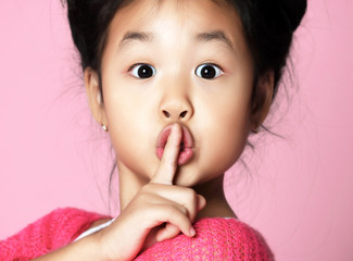 Asian kid girl in pink sweater shows shhh quiet sign on pink