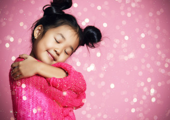 Obraz na płótnie Canvas Asian kid girl with closed eyes in pink sweater hug herself and dream. golden spangles