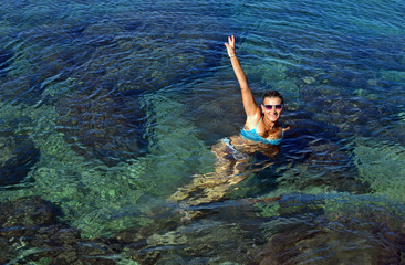 A young woman in swimsuit floats in seawater