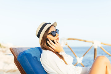 Beautiful happy girl talking on phone on a sea coast lying in lounge