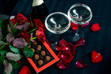 Obraz na płótnie Canvas two glasses of champagne, red roses, petals and chocolates on a black background