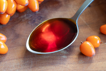 Sea buckthorn oil on a spoon with fresh sea buckthorn berries