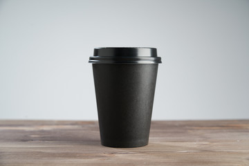 Black Paper coffee cup disposable for take away or to go, at wooden table, space for design layout.