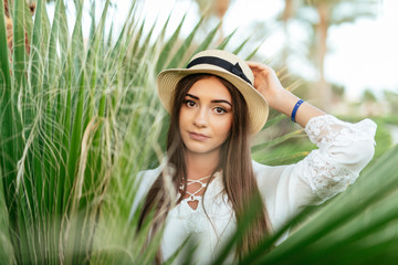 Portrait of happy young women smiling and posing, wearing straw hat in palm leaf background