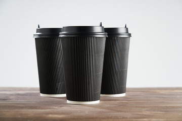Three Paper disposable coffee black cup for take away or to go, at wooden table, space for design layout.