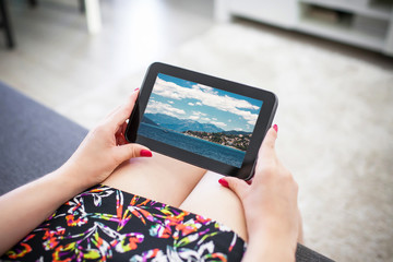 Watching holiday photos on black tablet. Summer sea sunny day landscape on device screen.