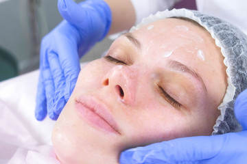 Obraz na płótnie Canvas Beautician puts the cream on the woman's face. Cosmetologist facial treatment. Close-up.