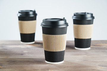 Three Paper disposable coffee black cup for take away or to go, at wooden table, space for design layout.