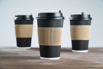 Three Paper disposable coffee black cup for take away or to go, at wooden table, space for design layout.