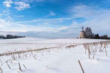 Empty Countryside Landscape in Sunny Winter Day with Snow Covering the Ground with Big Abandoned Windmill in Background