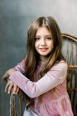 Beautiful little fashion model ongray background sits on the wooden chair close-up portrait