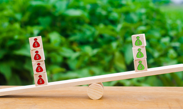 Cubes on scales with red patterns outweigh the money green. The concept of deficit, cost growth, business unprofitability. Pessimistic forecast, falling profits, outflow of investments and capital.