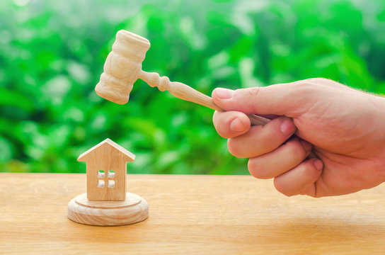 Elimination and alienation of bankruptcy, confiscation and nationalization. Decision of property disputes. The judge's hand is holding a hammer next to the wooden house. trial of real estate.