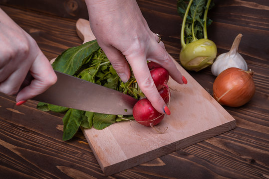 A woman's hand cuts radishes on a wooden board