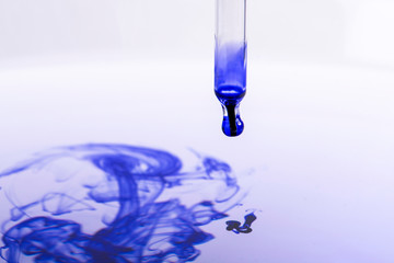 Pipette with blue liquid dripping into water
