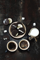 Two cups of espresso, a jug of milk and chocolate chip cookies with a white filling. Stylish shabby background. Coffee breakfast for two.