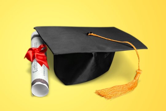 Graduation hat and diploma on yellow background