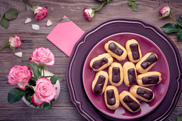 Mini vanilla eclairs with chocolate frosting on purple plate, top view on rustic wooden table