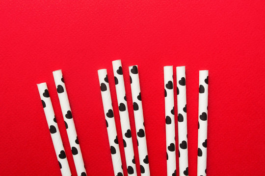 White Paper Straw With Black Hearts Over Red Background