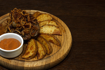 copy spaсe, steak with fried onions, potatoes and sauce. On a wooden board
