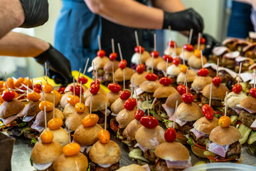 Female and Male Chef Putting Ingredients of Burgers on a Sliced Bread Spread on a Table in Black Gloves - Concept of the Hard Working Person and the Hygiene in the Kitchen
