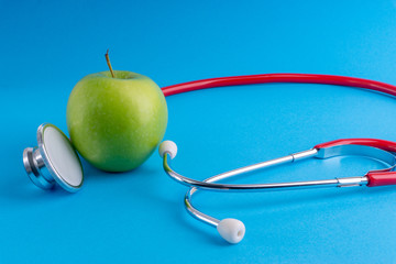 Green Apple with medical stethoscope isolated on blue background for healthy eating. Selective focus and crop fragment. Healthy, Diet and copy space concept
