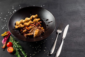 A meat dish with bread sticks and spices on black background