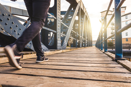Man walking alone over a bridge at sunset
