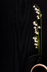 Lilies of the valley and black coffee on a black wooden background, top view, composition of black and white